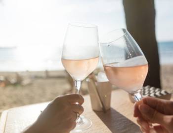 two glasses of rose wine toast with beach sand in the background