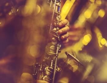 artsy image of person playing a saxophone with view on hands and the neck of the sax and blurry lights around it