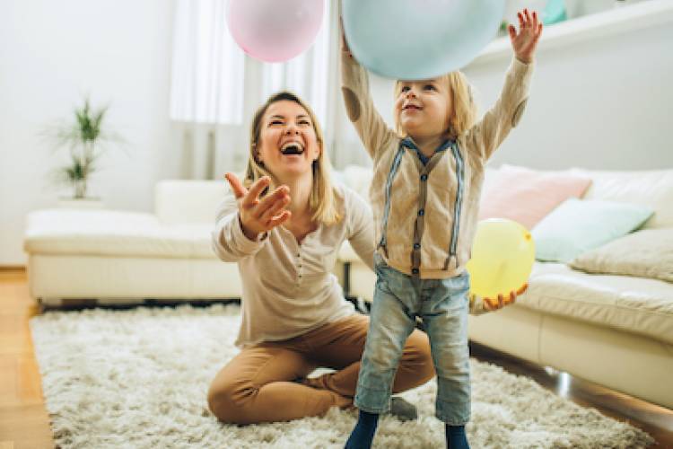 Happy mother and her small son playing with a balloons at home. Focus is on boy