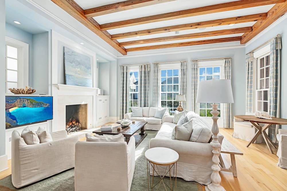 interior shot of luxury beach house featuring cozy white couches, fireplace and tall beamed cealings