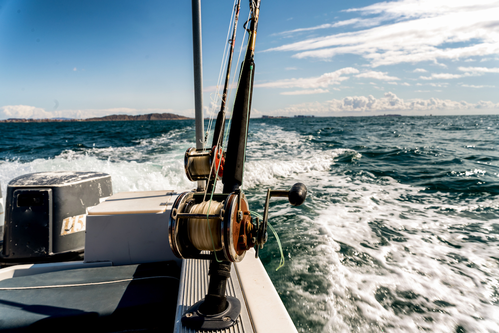 fishing pole anchored on yacht with wake in the background