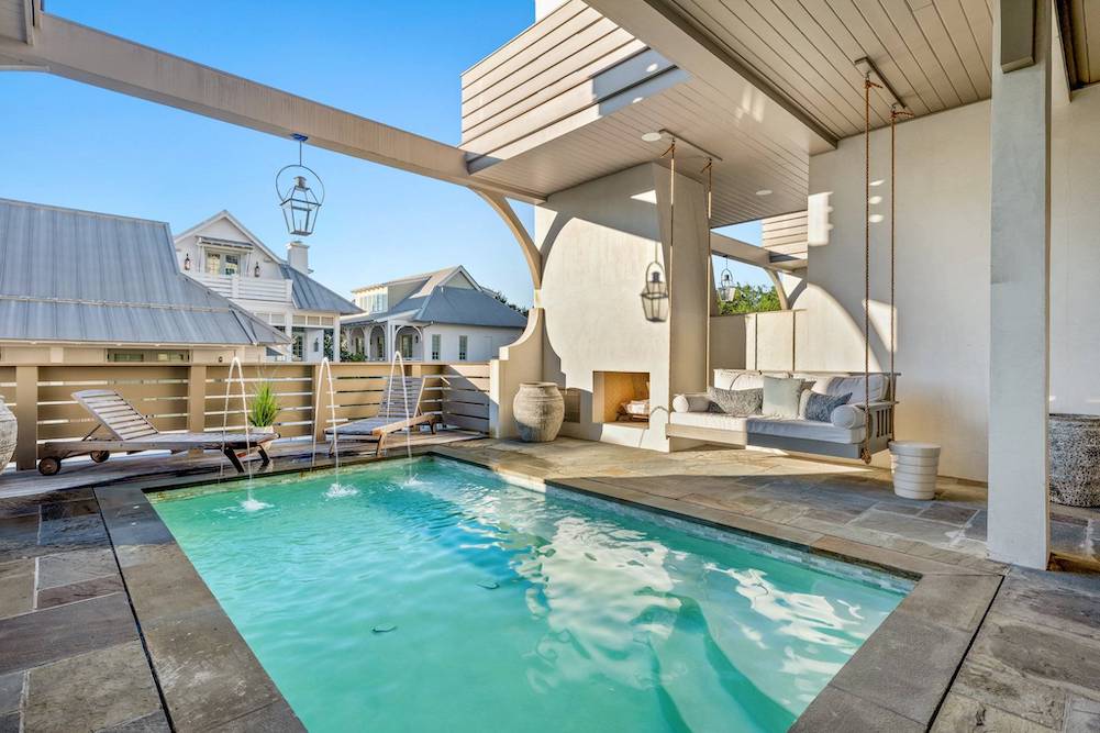 Image of a swimming pool with fountains spraying into the back of it and a luxurious daybed swings under a covered porch