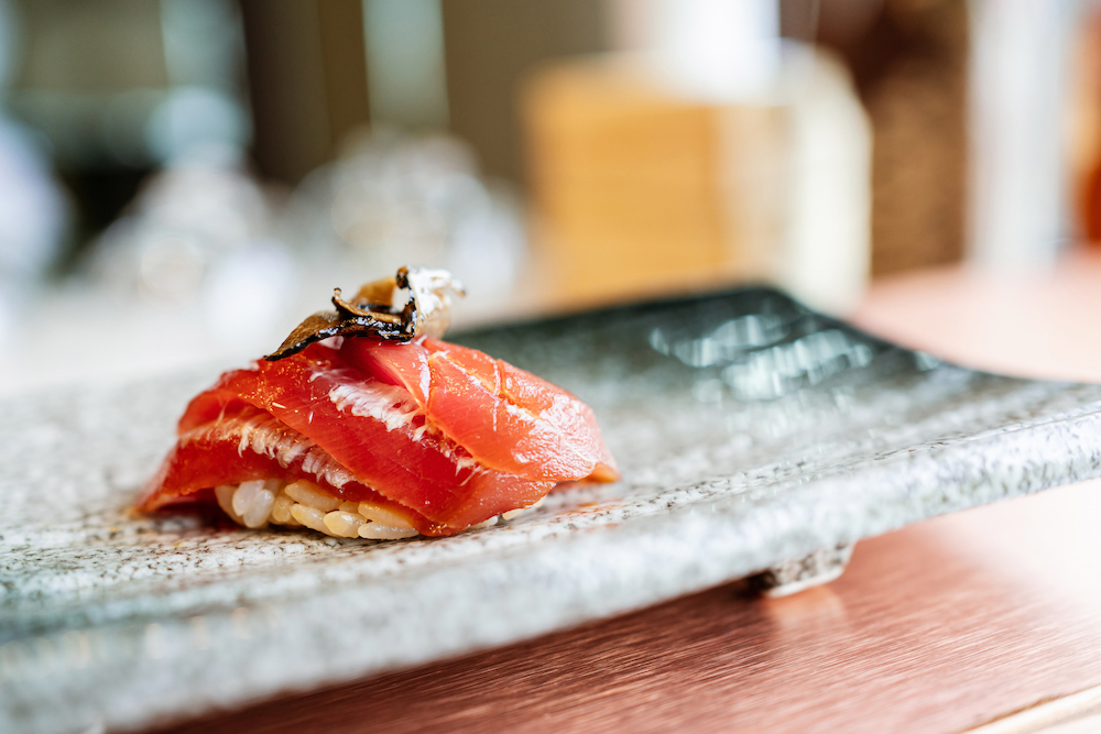 Japanese Omakase meal: Aging Raw Akami Tuna Sushi adds with sliced truffle served by hand on a stone plate
