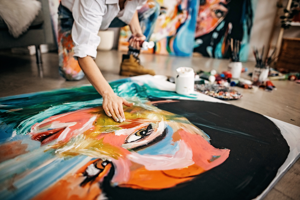 person painting on large canvas on the ground in an art studio