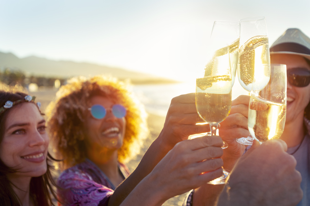 four friends cheers with glasses of white wine on the beach at sunset