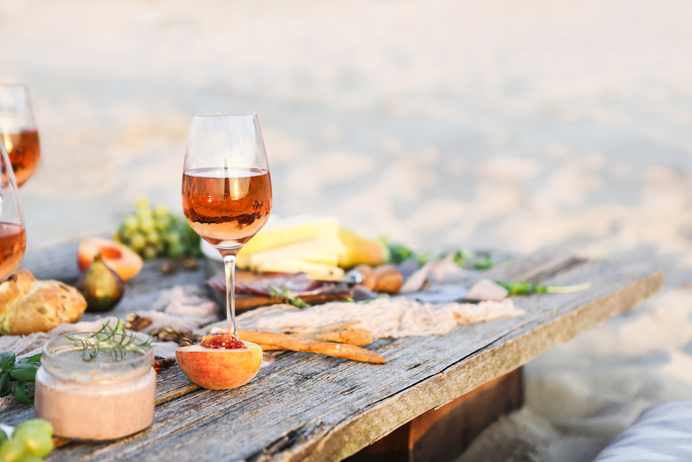 rustic board set on the sand with fruit and a glass of wine on it
